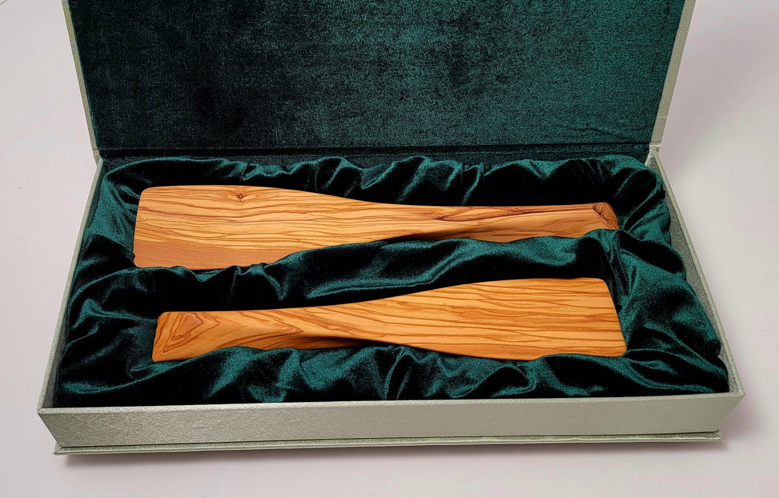 Two olive wood spatulas nestled in dark green velvet packaging inside a sage green presentation box.
